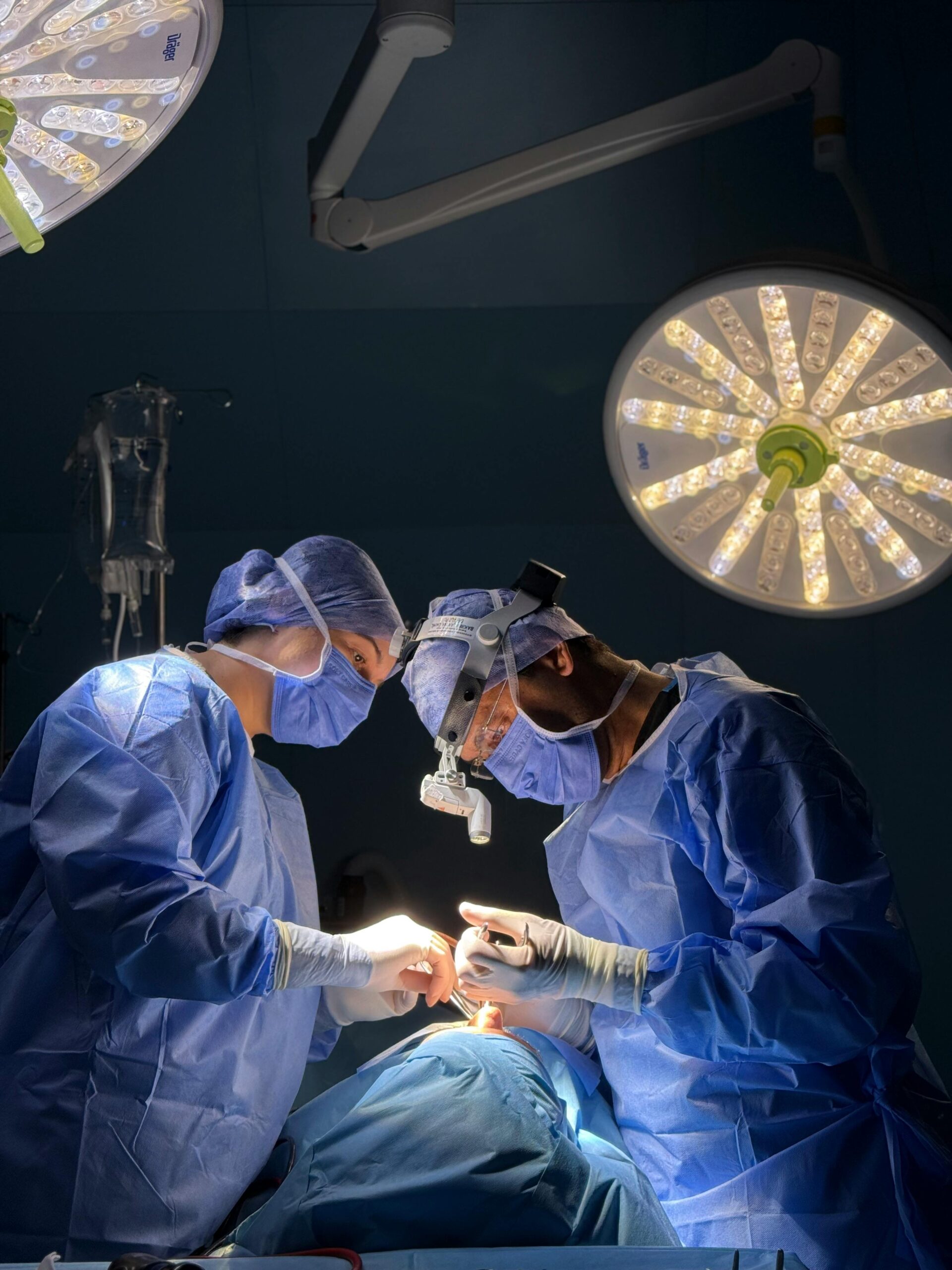 Surgeons in blue scrubs focus intensely during a critical operation under bright lights.